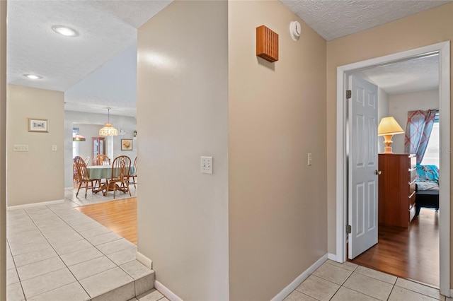 hallway featuring light tile patterned floors, plenty of natural light, baseboards, and a textured ceiling