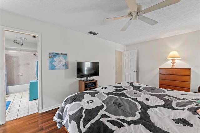 bedroom featuring a textured ceiling, ensuite bathroom, wood finished floors, visible vents, and baseboards