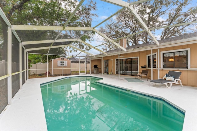 view of swimming pool with an outbuilding, a patio, glass enclosure, a fenced backyard, and a shed