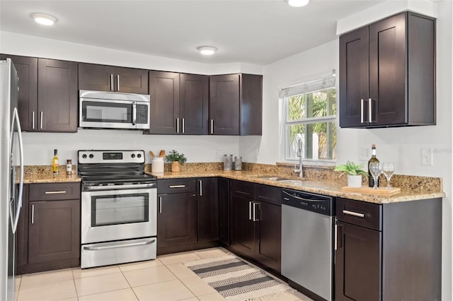 kitchen with light tile patterned floors, light stone counters, stainless steel appliances, a sink, and dark brown cabinets