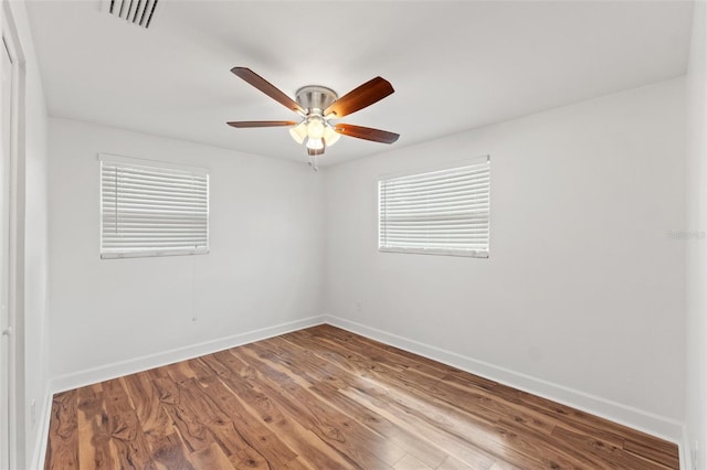 spare room with a ceiling fan, wood finished floors, visible vents, and baseboards