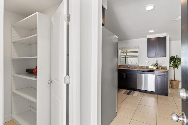 interior space with light tile patterned floors, light stone counters, dark brown cabinetry, a sink, and appliances with stainless steel finishes