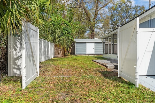 view of yard featuring an outbuilding, a storage unit, a fenced backyard, and a sunroom