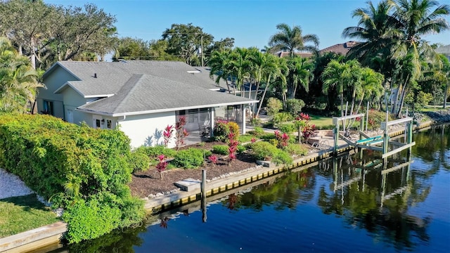 exterior space featuring stucco siding, a water view, boat lift, and roof with shingles