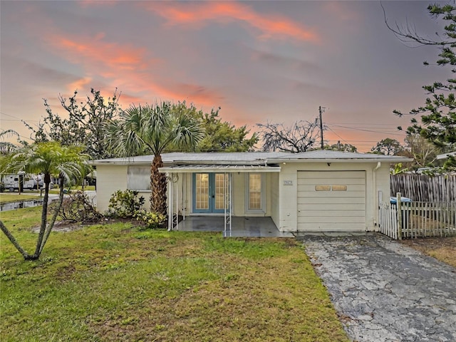 back of property featuring french doors, a lawn, an attached garage, fence, and driveway