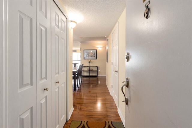 corridor featuring a textured ceiling, baseboards, and wood finished floors