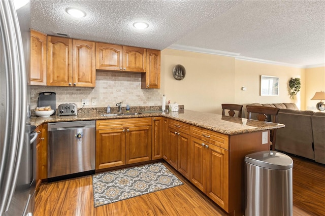 kitchen featuring stainless steel appliances, light wood-type flooring, a sink, and light stone countertops