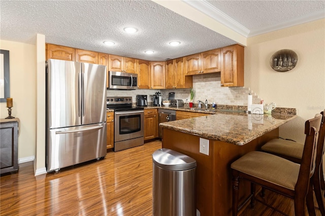 kitchen with stainless steel appliances, tasteful backsplash, a sink, wood finished floors, and a peninsula