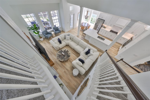 living room with a towering ceiling, ornate columns, light wood-style flooring, and stairway