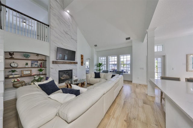 living area with visible vents, baseboards, a towering ceiling, light wood-style flooring, and a fireplace