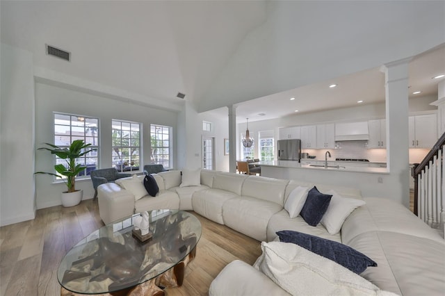 living area with decorative columns, visible vents, an inviting chandelier, light wood-style floors, and high vaulted ceiling