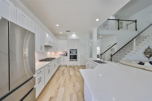 kitchen featuring stainless steel appliances, premium range hood, a sink, white cabinetry, and light wood-style floors