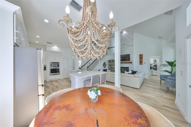 dining room featuring stairway, independent washer and dryer, light wood-style floors, a chandelier, and a high end fireplace