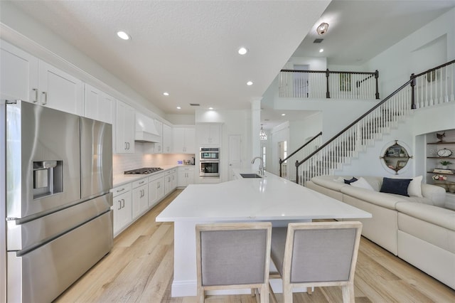 kitchen featuring open floor plan, stainless steel appliances, white cabinets, and light wood-style floors