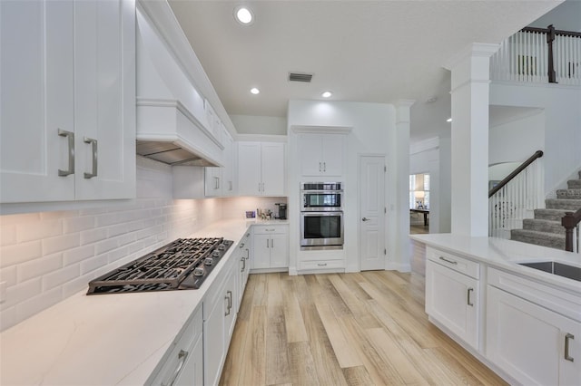 kitchen with stainless steel double oven, gas cooktop, light wood-style flooring, visible vents, and tasteful backsplash