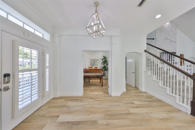 interior space featuring arched walkways, light wood-style flooring, visible vents, stairway, and an inviting chandelier