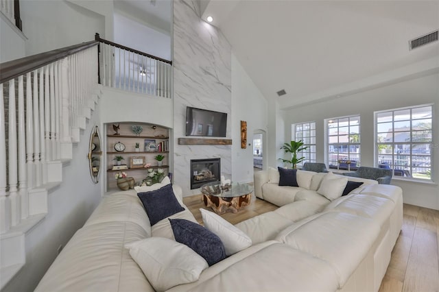 living room featuring visible vents, high vaulted ceiling, wood finished floors, and a high end fireplace