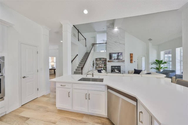 kitchen featuring a large fireplace, a sink, white cabinets, open floor plan, and dishwasher