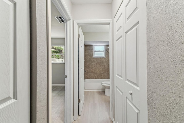 hallway featuring visible vents, a textured wall, and light wood-style flooring