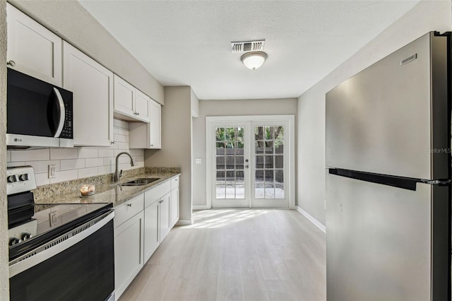 kitchen with a sink, white cabinetry, visible vents, appliances with stainless steel finishes, and light stone countertops