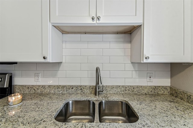 kitchen featuring light stone countertops, tasteful backsplash, white cabinetry, and a sink