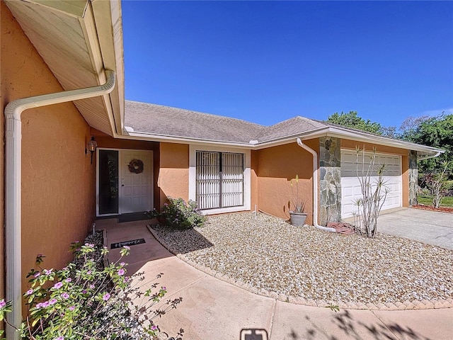 view of exterior entry with stucco siding, driveway, a shingled roof, and a garage