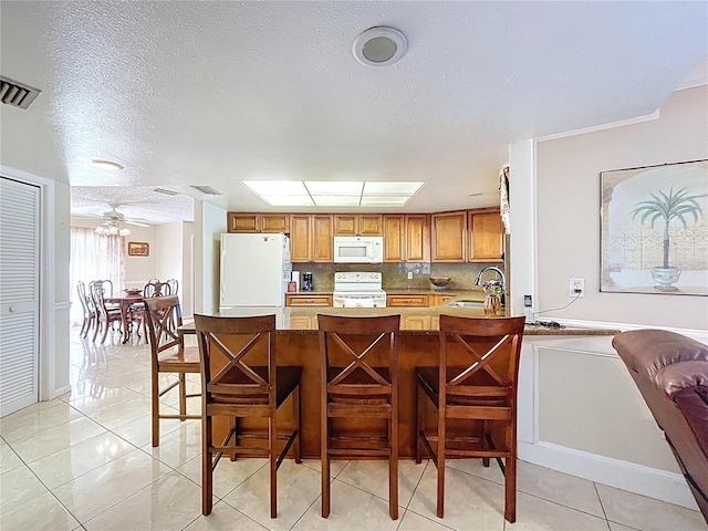 kitchen with visible vents, brown cabinets, a sink, tasteful backsplash, and white appliances