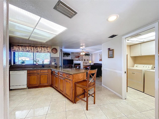 kitchen featuring a fireplace, separate washer and dryer, a sink, dishwasher, and brown cabinets