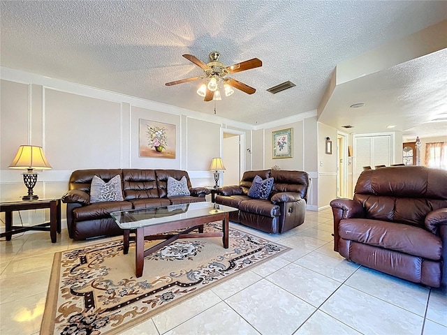 living room with visible vents, a textured ceiling, light tile patterned flooring, a decorative wall, and ceiling fan