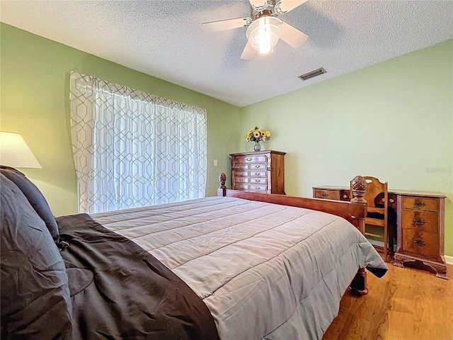 bedroom featuring visible vents, a textured ceiling, a ceiling fan, and wood finished floors