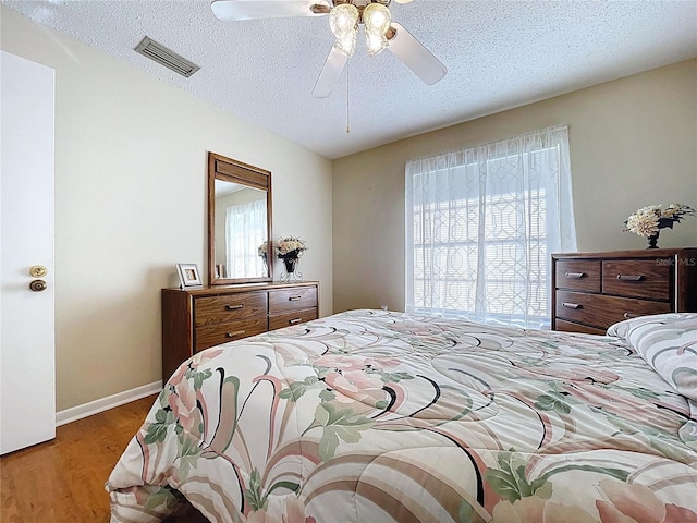 bedroom with a ceiling fan, baseboards, wood finished floors, visible vents, and a textured ceiling