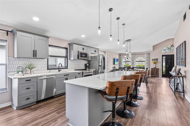31123 Stone Arch Ave, Wesley Chapel, FL 33545 - kitchen featuring stainless steel appliances, backsplash, gray cabinetry, a kitchen island, and a kitchen bar