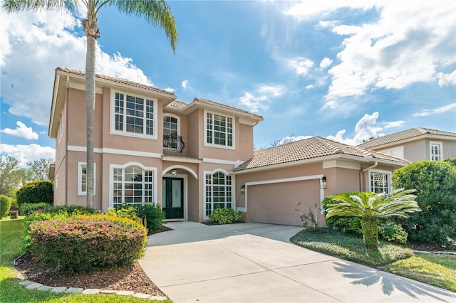 mediterranean / spanish-style house with a garage, concrete driveway, a tile roof, and stucco siding