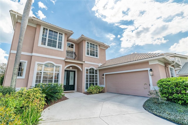 mediterranean / spanish home with an attached garage, a balcony, driveway, a tiled roof, and stucco siding