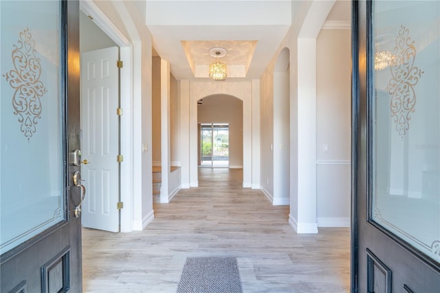 foyer with arched walkways, a tray ceiling, light wood-type flooring, and baseboards