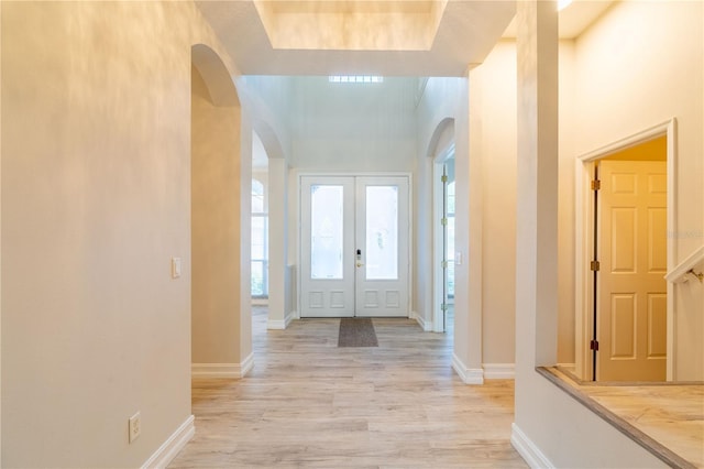 foyer with plenty of natural light, arched walkways, light wood-style flooring, and baseboards