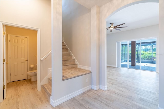 staircase featuring a ceiling fan, baseboards, arched walkways, and wood finished floors