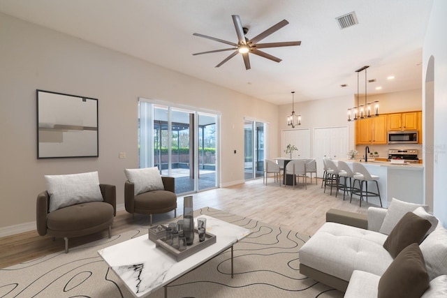 living area featuring baseboards, visible vents, light wood finished floors, and ceiling fan with notable chandelier