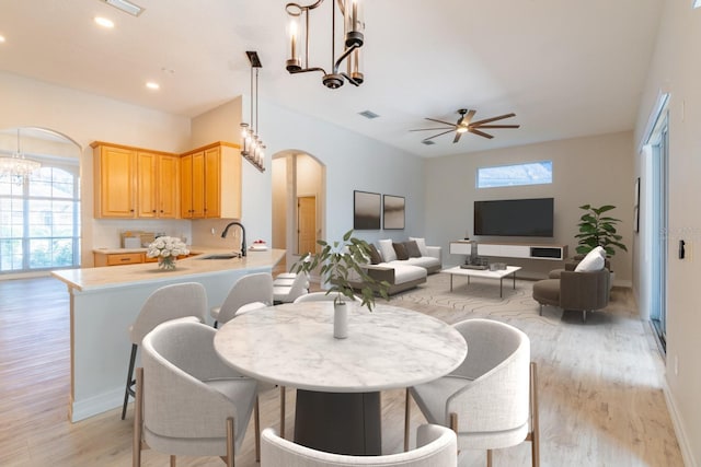 dining space with arched walkways, baseboards, light wood-style flooring, ceiling fan with notable chandelier, and recessed lighting