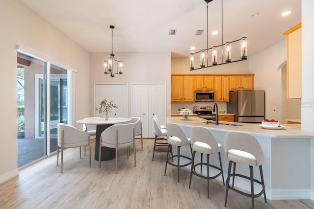 kitchen featuring a breakfast bar, stainless steel appliances, light countertops, light wood-style flooring, and a sink