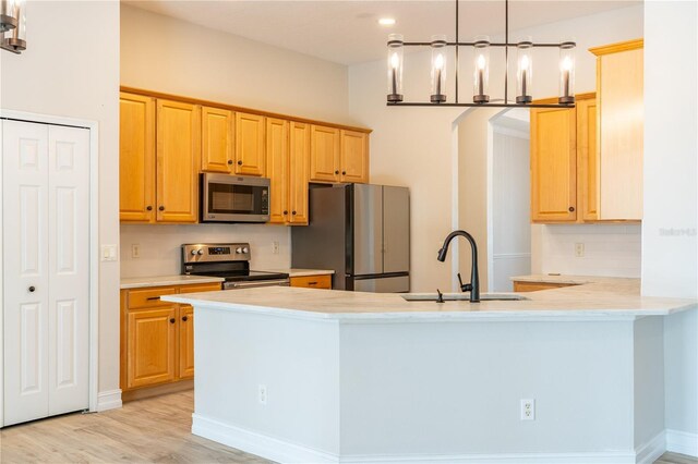 kitchen featuring appliances with stainless steel finishes, a peninsula, light countertops, light wood-type flooring, and a sink