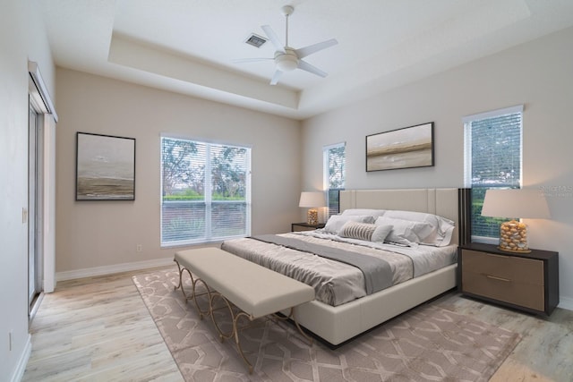 bedroom with a tray ceiling, ceiling fan, light wood-style flooring, and baseboards