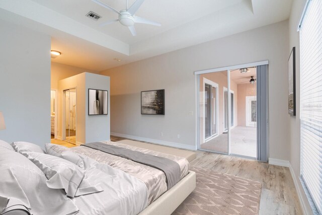 bedroom with visible vents, baseboards, access to outside, a tray ceiling, and light wood-style floors