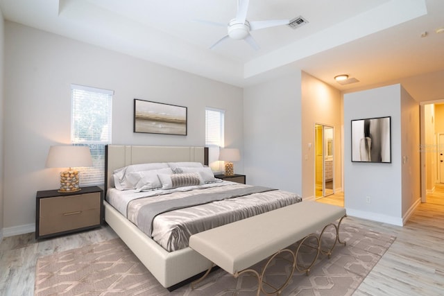 bedroom featuring light wood-type flooring, visible vents, multiple windows, and a tray ceiling