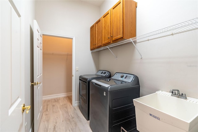 laundry area featuring cabinet space, light wood finished floors, baseboards, washer and clothes dryer, and a sink