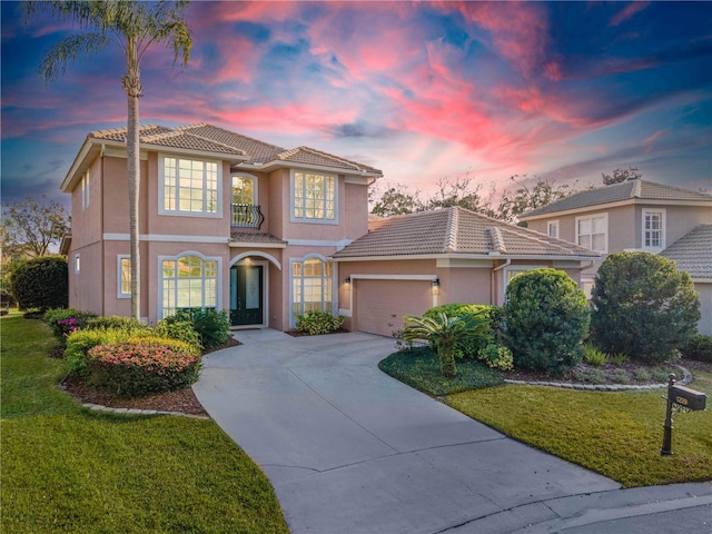 mediterranean / spanish home featuring driveway, a lawn, a tiled roof, an attached garage, and stucco siding