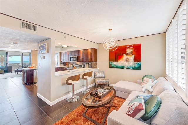 living room with a textured ceiling, dark tile patterned flooring, visible vents, baseboards, and an inviting chandelier