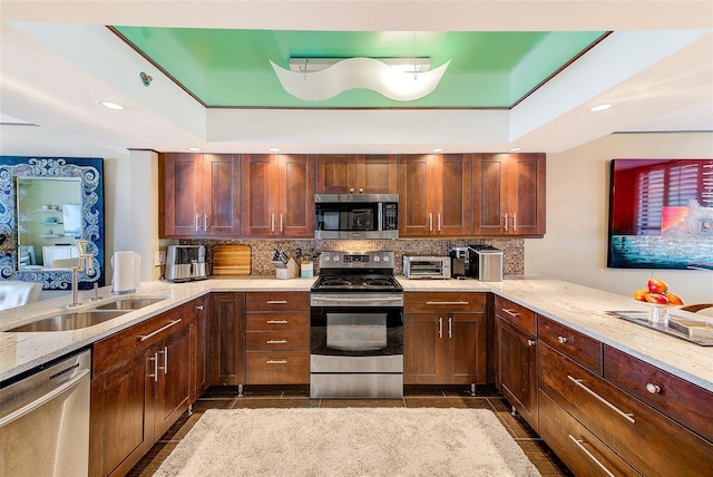 kitchen with tasteful backsplash, a raised ceiling, a peninsula, stainless steel appliances, and a sink