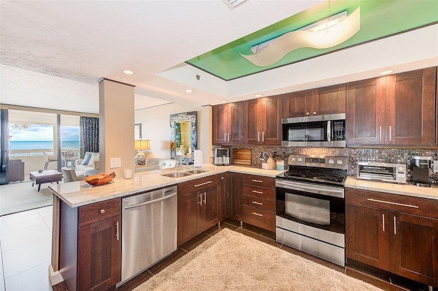 kitchen with appliances with stainless steel finishes, light stone counters, a peninsula, and decorative backsplash