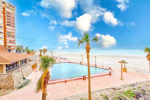 community pool featuring a water view, fence, and a beach view